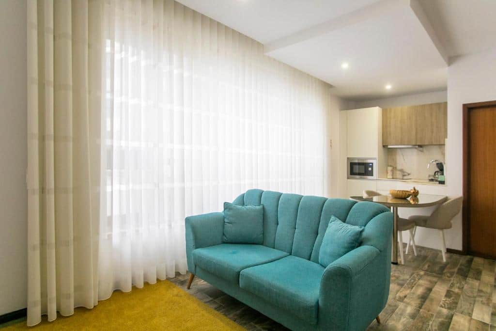 Sala de estar da Casa de Cristal, com sofá azul-claro em primeiro plano e, ao fundo, uma mesa com cadeiras e armários de cozinha.