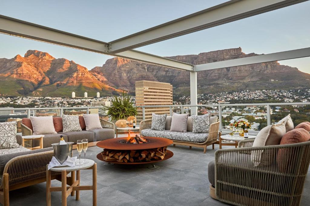 Lounge exterior moderno no Taj Cape Town com sofás e uma fogueira, com vista para a cidade e as montanhas ao pôr do sol.