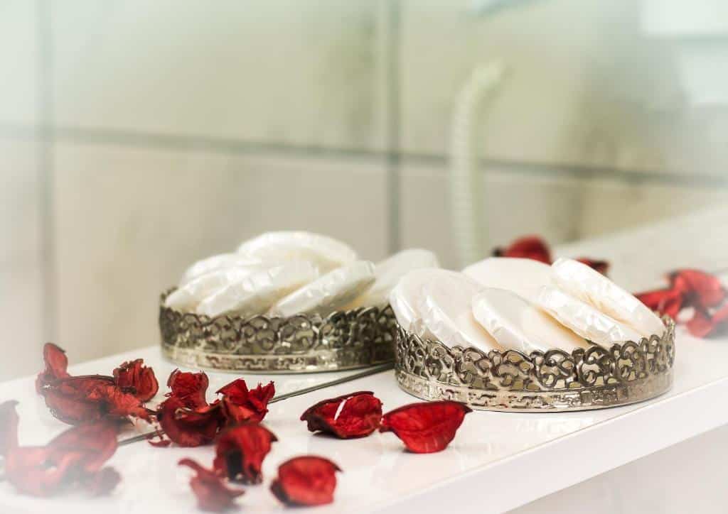 Duas bandejas ornamentadas do Zeyn Otel Istanbul com sabonetes brancos embrulhados, sobre uma superfície branca rodeada de pétalas vermelhas secas.