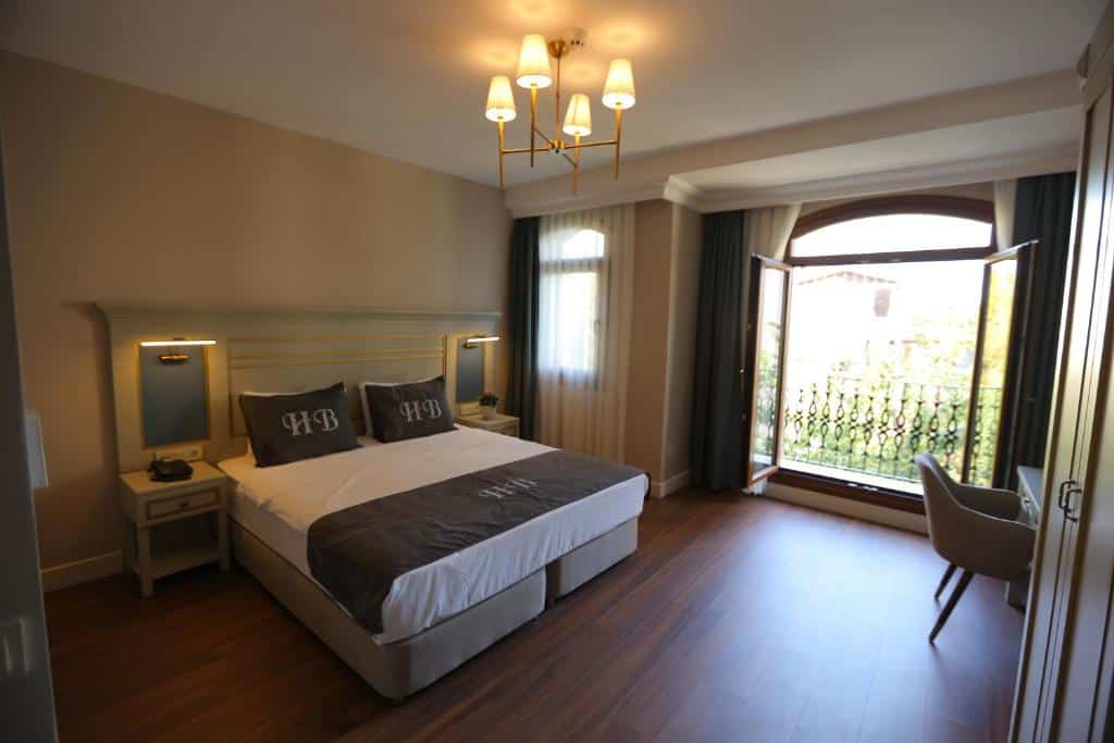Uma cama de casal do HaciBayramHotel bem arrumada num quarto com pavimento de madeira, mesas de cabeceira e uma janela aberta com vista.