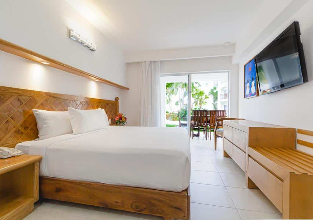 Quarto no Beachscape Kin Ha Villas & Suites com varanda extensa com cadeiras, cama de casal, cómoda e televisão, tudo em madeira e roupa de cama branca