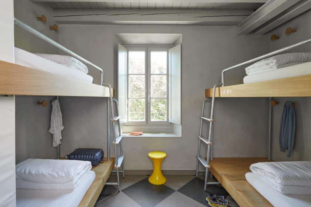 Quarto do Combo Milano com dois beliches e uma janela ao centro, com espaço entre os beliches para guardar a mala