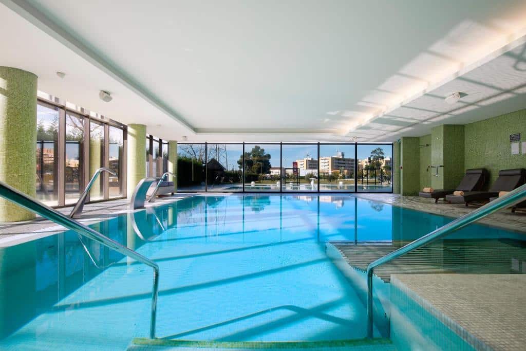 Piscina coberta do Meliá Braga Hotel & Spa, com cadeirões ao lado.