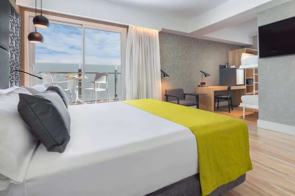 Quarto do Catalonia Giralda com cama de casal, televisão e uma varanda com mesa e cadeiras ao fundo.