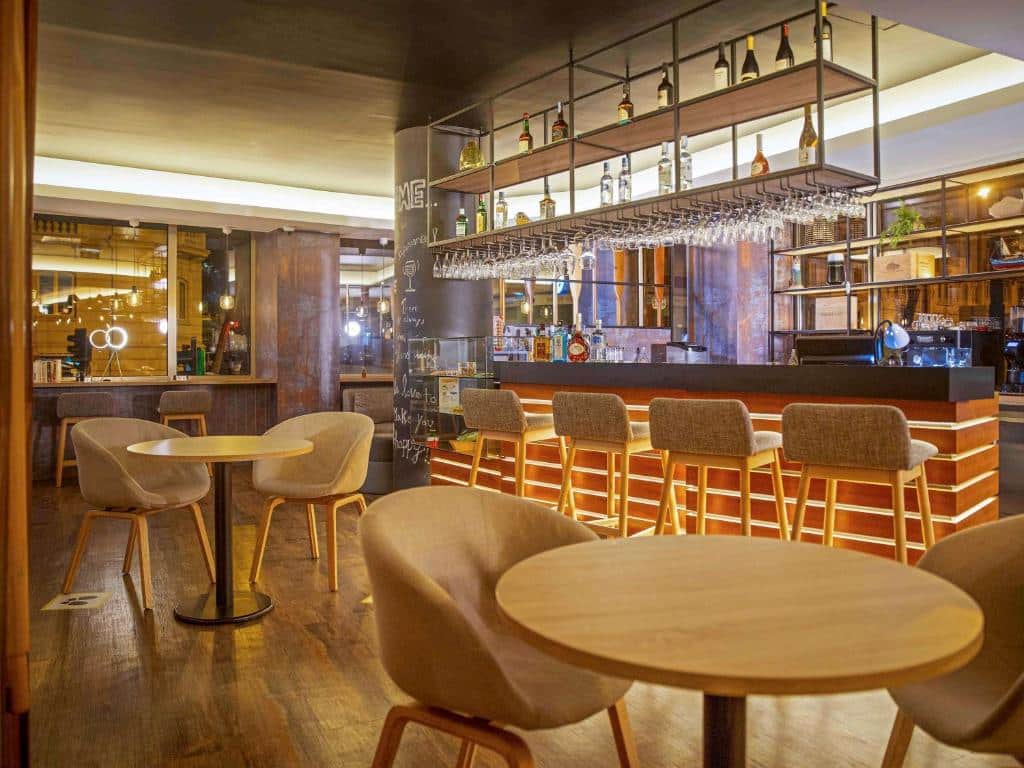 Interior do bar moderno do Ibis Styles Lisboa Centro com mesas e cadeiras de madeira e iluminação acolhedora.