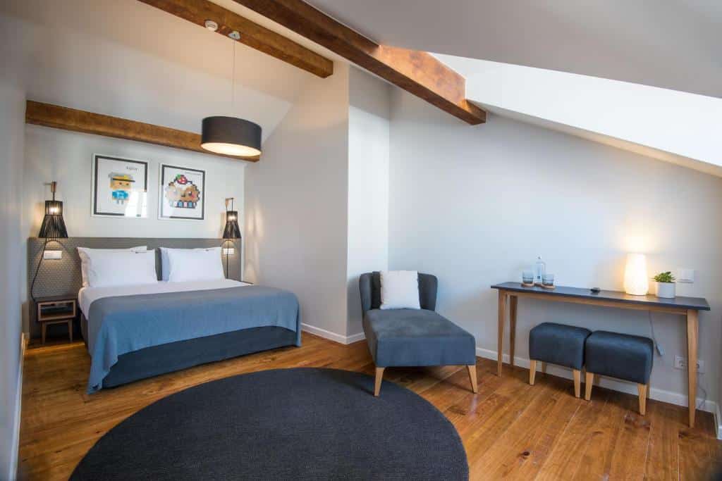 Quarto do Urbano FLH Hotels Lisboa com bom espaço interior, uma cama de casal com candeeiros suspensos nas laterais, um tapete redondo, uma mesa com pufes e um cadeirão estofado