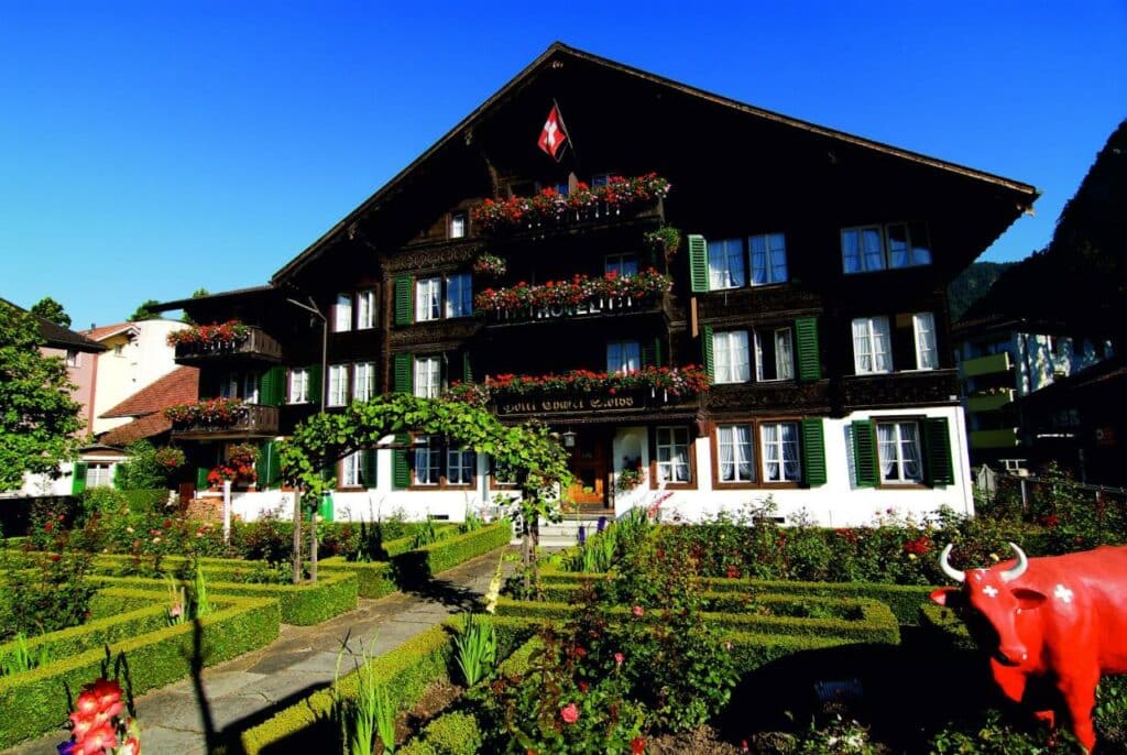 Fachada do Hotel Chalet Swiss em estilo alpino, com jardim em frente.
