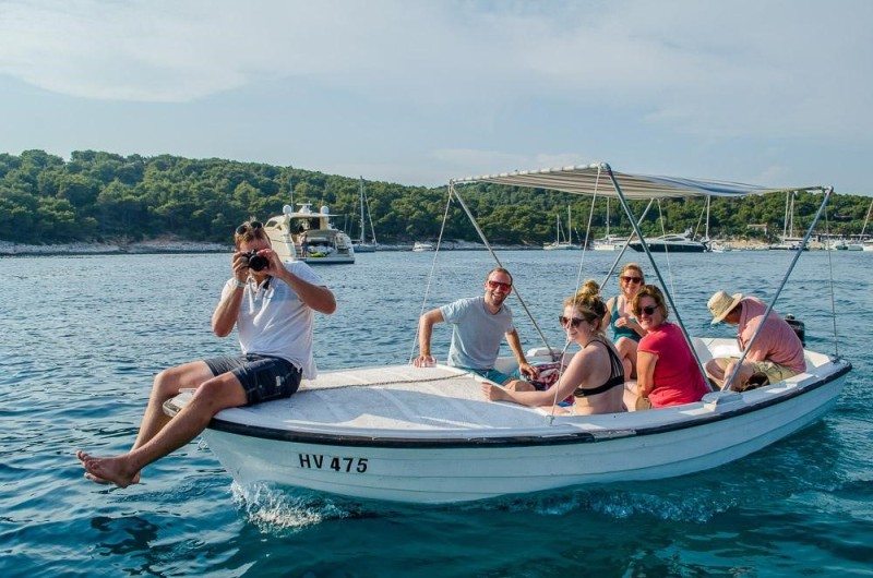Um grupo de pessoas sentado num pequeno barco a motor com cobertura, numa zona costeira tranquila, rodeado de outros barcos e de uma costa arborizada.