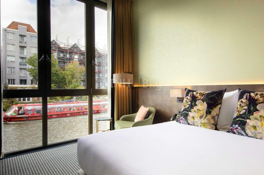 Quarto do Monet Garden Hotel Amsterdam com cama de casal, um cadeirão e janela ampla com vista para um canal e um barco