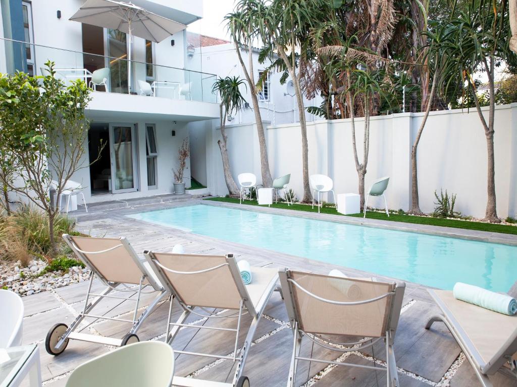 Pátio moderno do Zest Boutique Hotel com piscina retangular, espreguiçadeiras, mesas e uma casa branca de dois pisos ao fundo.