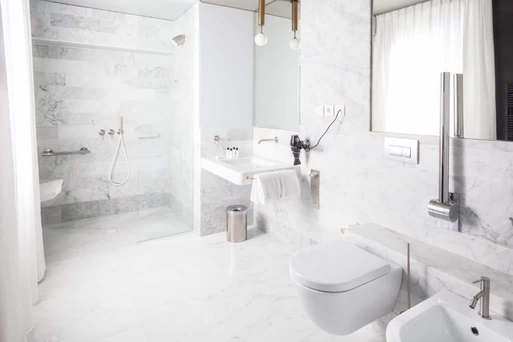 Casa de banho adaptada do Senato Hotel Milano com uma cabine de duche com barras de apoio e sem porta de vidro, lavatório mais baixo e mais barras de apoio junto à sanita