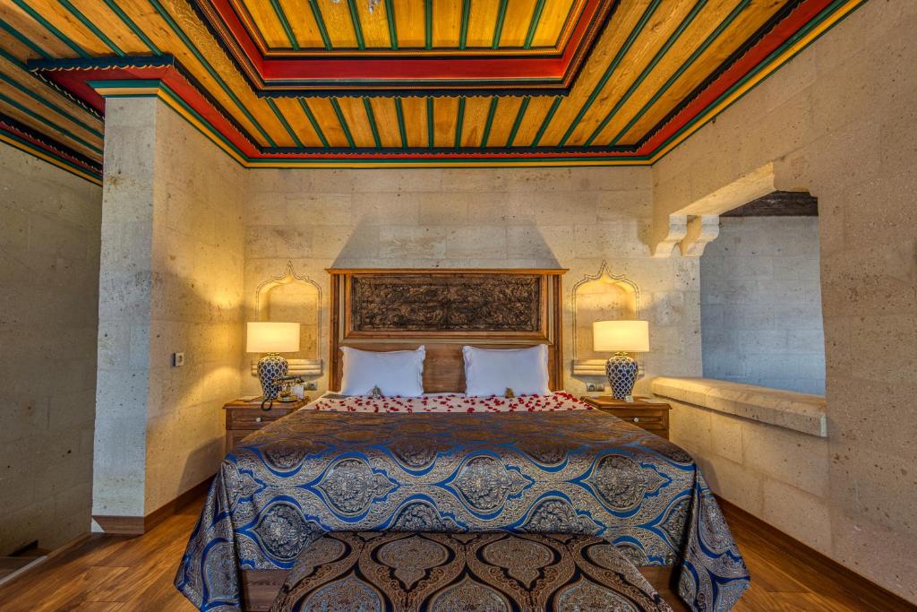 Cama de casal no Museum Hotel, um dos hotéis da Capadócia, com colcha azul estampada, candeeiros e cabeceira de madeira trabalhada num quarto com paredes de pedra.