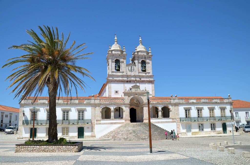 Igreja de Nossa Senhora da Nazaré, com fachada imponente e duas torres sineiras simétricas, à frente de uma praça em calçada portuguesa.