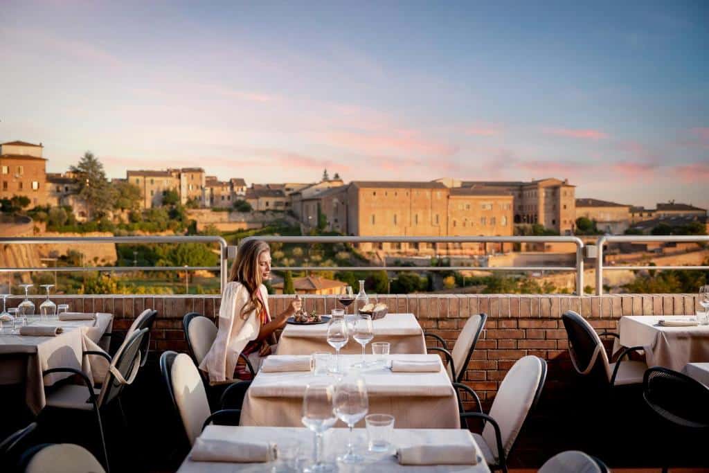 Mulher a jantar num restaurante com vista panorâmica sobre cidade histórica italiana ao entardecer