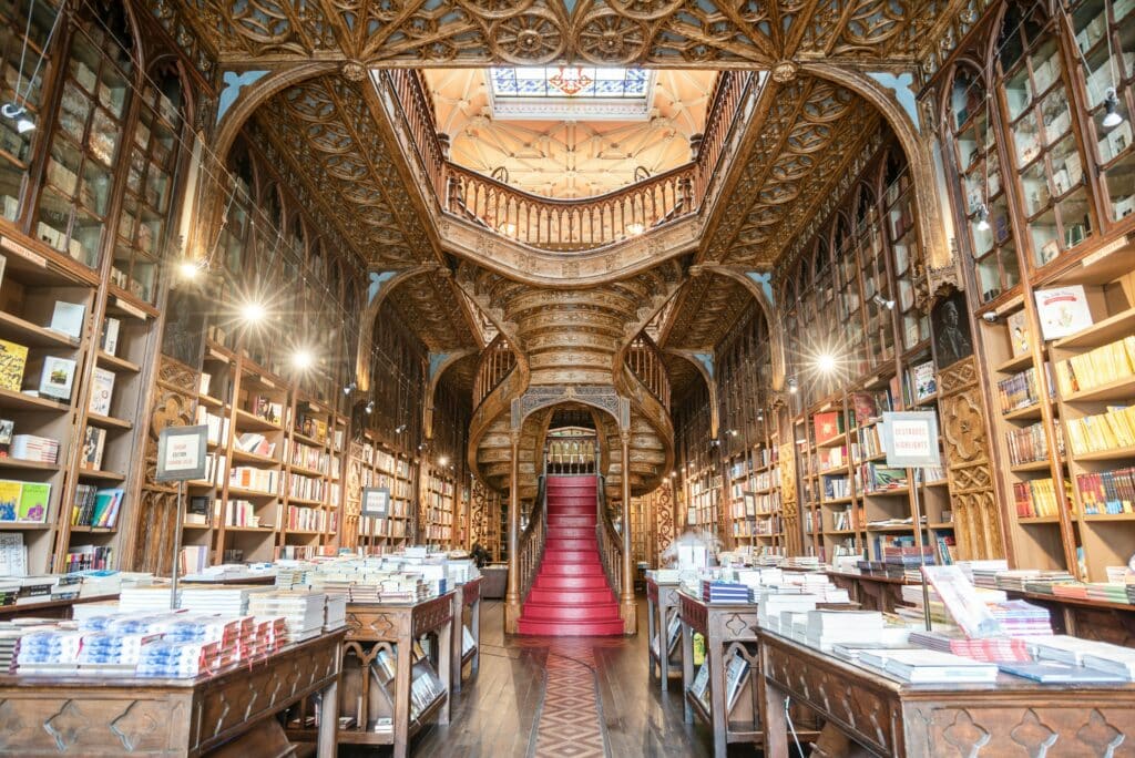 Interior da Livraria Lello, com estantes de livros de cada lado e a escadaria que dá acesso ao piso superior ao fundo.