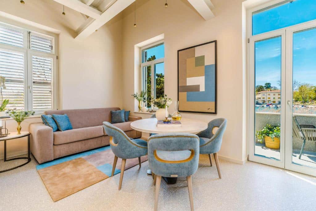 Sala de estar moderna com sofá bege, mesa redonda e vista para área exterior ensolarada, na Villa Ghisi Apartments, em Kolovare