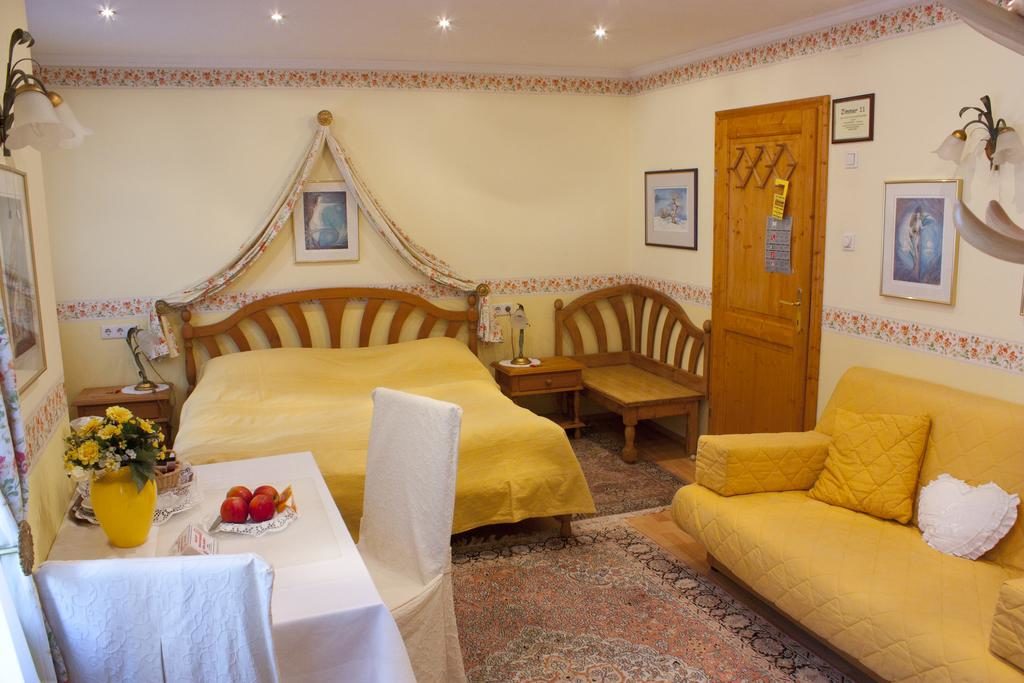 Quarto do Hotel Schneider-Gössl, com cama, mesa com um vaso de flores e fruta, cadeiras, sofás e um ambiente acolhedor.
