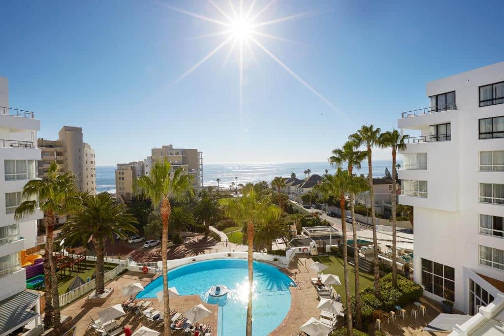 Piscina circular ao ar livre com espreguiçadeiras, palmeiras e edifícios brancos no President Hotel, sob um céu limpo.