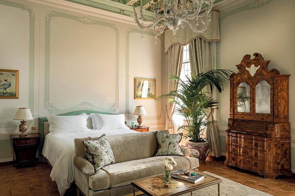 Quarto elegante com móveis antigos, cortinas e candeeiro de cristal, num ambiente acolhedor