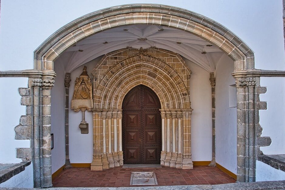 Entrada de igreja com portal de pedra e escultura. Ilustra este artigo sobre o que fazer em Évora.