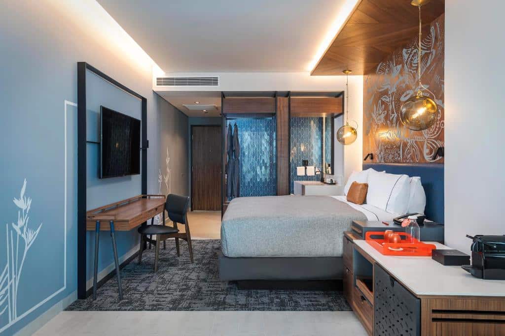 Quarto elegante no Canopy By Hilton Cancun La Isla decorado em tons de cinzento e azul, com cama de casal, secretária, televisão, varanda ampla e máquina de café