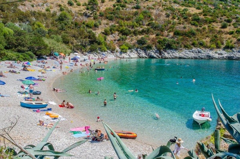 A praia pitoresca de Dubovica, em Hvar, com águas cristalinas azul-turquesa, banhistas a apanhar sol, a nadar e em pequenos barcos, rodeada de vegetação.