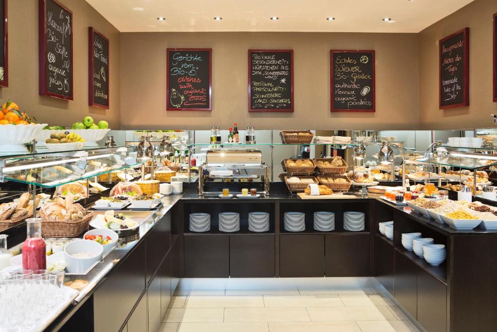Buffet de pequeno-almoço no The Harmonie Vienna, com vários alimentos, pães, fruta e ementas em ardósia, numa zona de refeições bem iluminada.