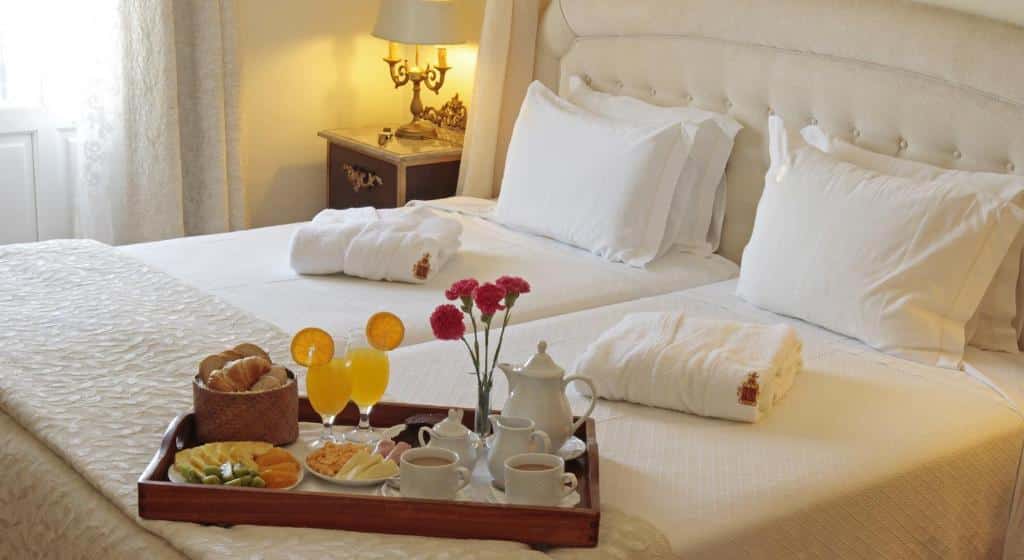 Cama de um dos quartos do Hotel Real d'Óbidos com roupa branca e tabuleiro de pequeno-almoço com pães e fruta