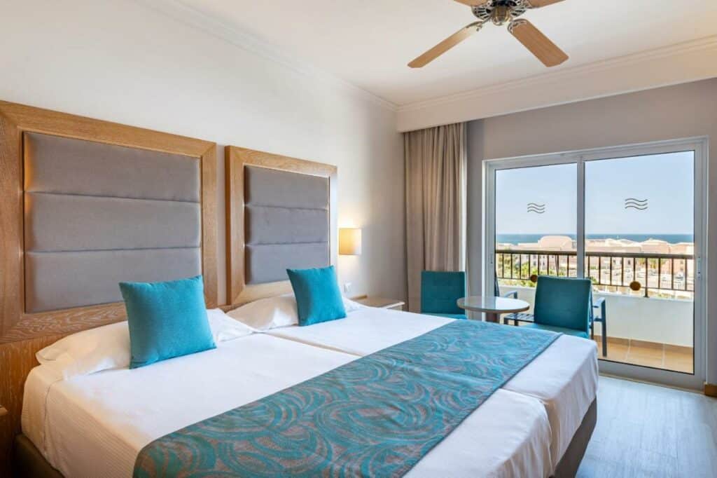 Quarto do 3HB Guarana – All Inclusive com cama de casal do lado esquerdo da imagem, do lado esquerdo da cama duas poltronas com uma mesa redonda. Representa hotéis all inclusive em Portugal.