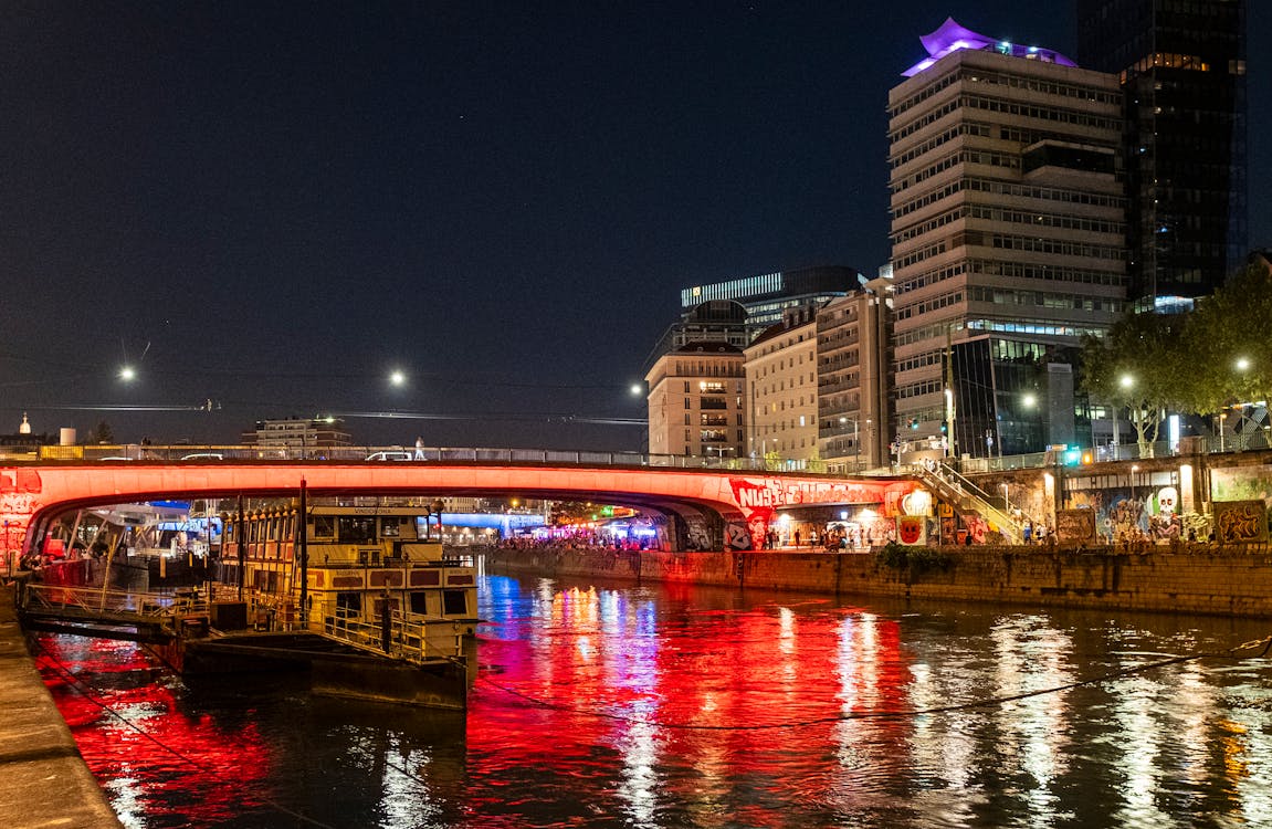 Vista noturna do canal do Danúbio, com pontes e edifícios iluminados e reflexos de luzes na água.