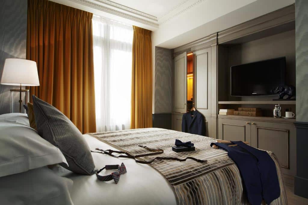 Quarto do La Maison Favart com cama, televisão, roupeiro e candeeiro.