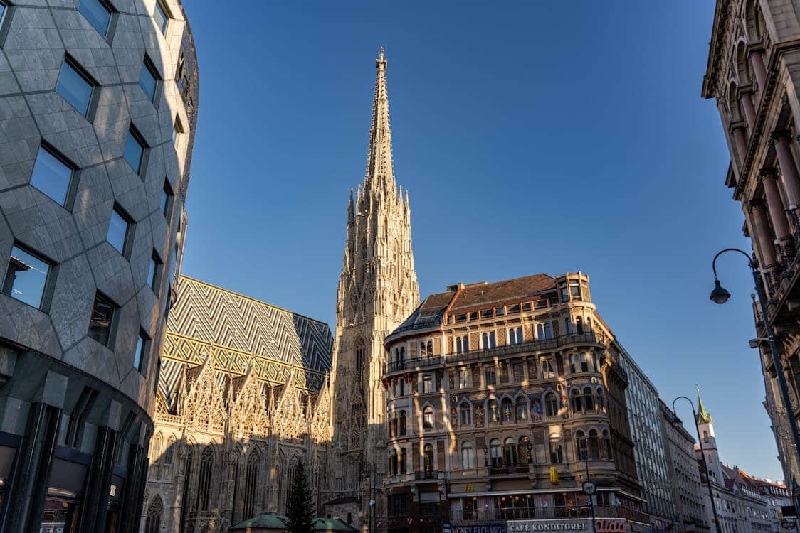 Catedral de Santo Estêvão vista de lado, com a sua torre detalhada a erguer-se entre edifícios históricos, sob céu azul.