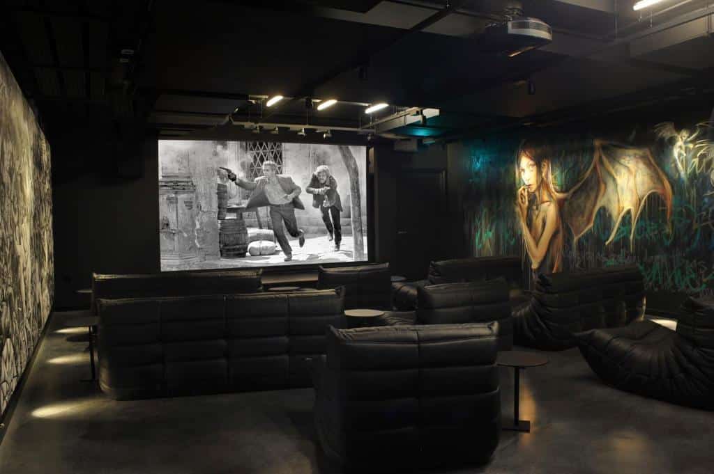 Sala de cinema com poltronas e sofás no The Mandrake, com paredes cheias de desenhos e um ecrã de cinema