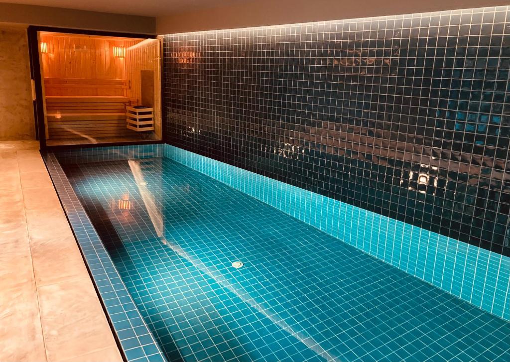 Piscina interior retangular com azulejos azuis ao lado de uma sauna com bancos de madeira e iluminação suave, na Pousada do Porto – Rua das Flores.