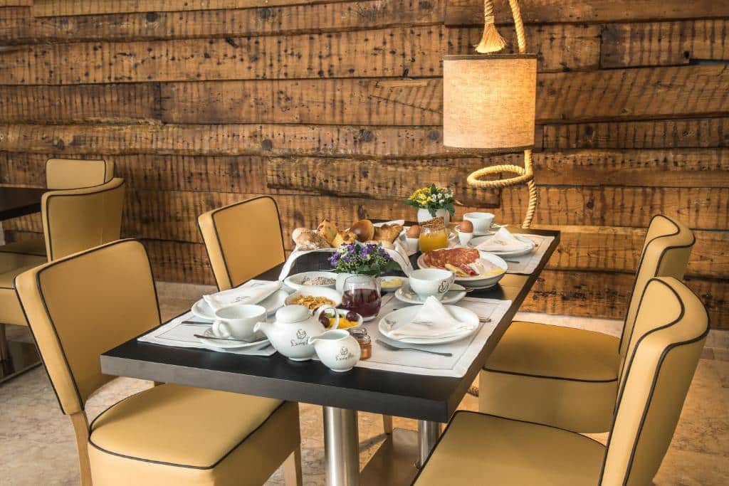 Mesa na sala de refeições do Lisboa Prata Boutique Hotel com vários itens de pequeno-almoço e dois pequenos vasos de flores, quatro cadeiras estofadas e um candeeiro ao lado