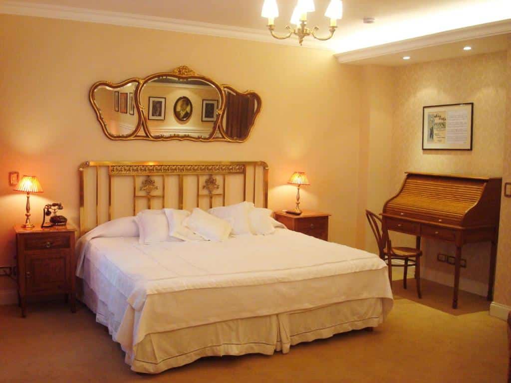 quarto do Tanguero Hotel Boutique Antique com cama de casal, mesas e candeeiros dos dois lados, mesa e cadeira de madeira e detalhes clássicos