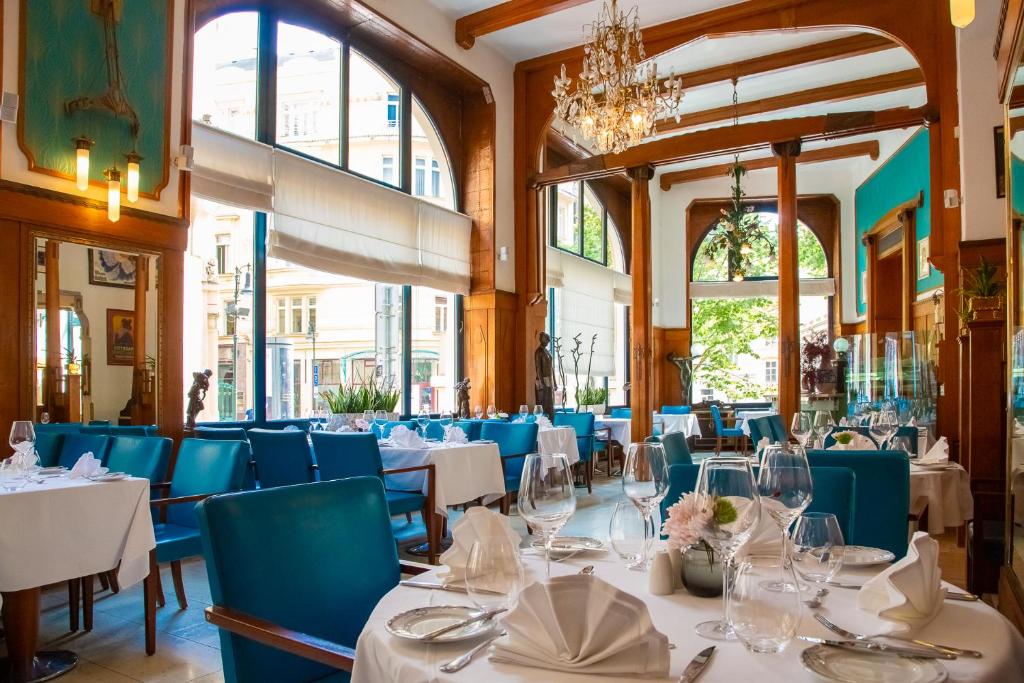 Sala de refeições do restaurante do Hotel Paris Prague, com cadeiras azuis, toalhas brancas, janelas grandes e lustres durante o dia.