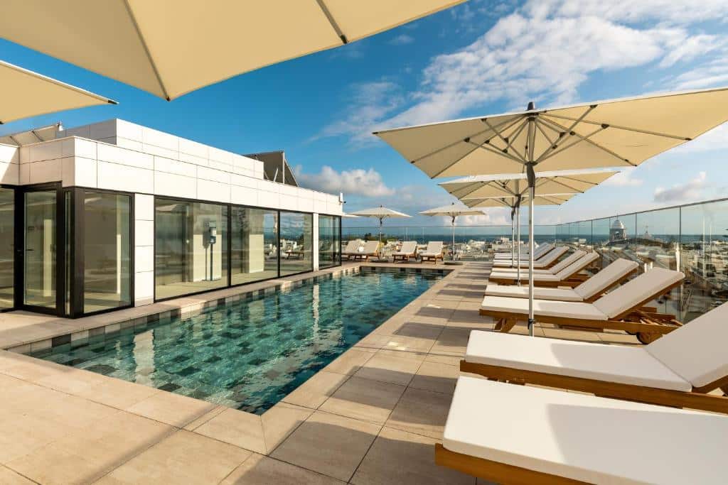 Piscina na cobertura com espreguiçadeiras e chapéus de sol, junto a um edifício moderno, sob um céu azul com nuvens dispersas, no Pure Formosa Concept Hotel em Olhão.