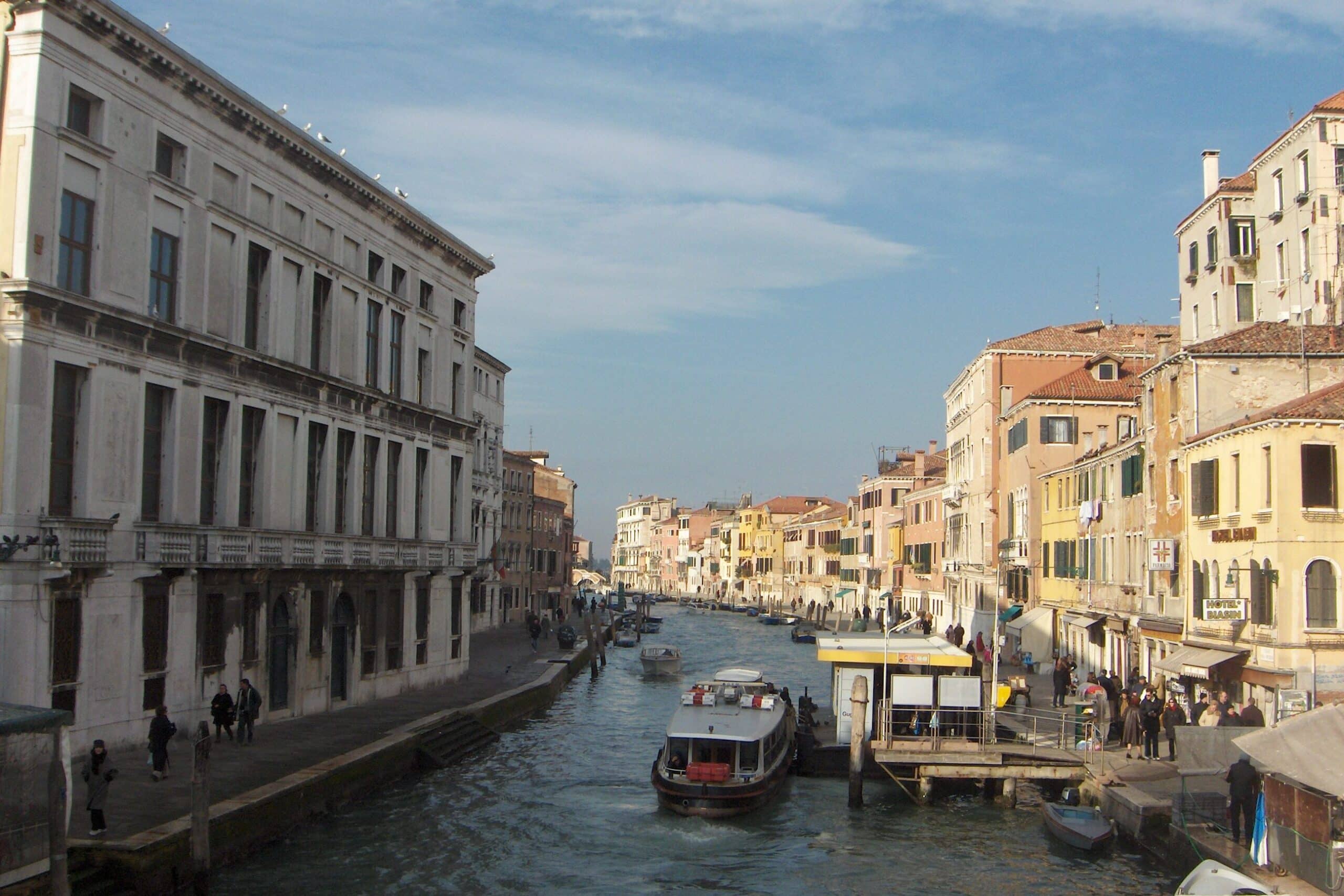 Edifícios históricos junto a um canal de Veneza, Itália, com barcos e pessoas a caminhar pelas margens