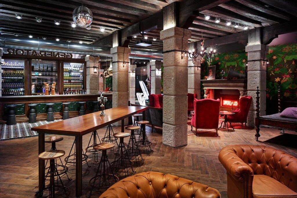 Bar acolhedor com mobiliário rústico e decoração típica, incluindo lustres, lareira e peças em madeira, com mesas e bancos altos