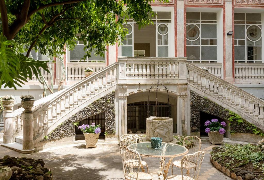 Edifício histórico de arquitetura clássica do Artemisia Domus, com escada exterior e fonte de água num jardim delimitado por plantas.