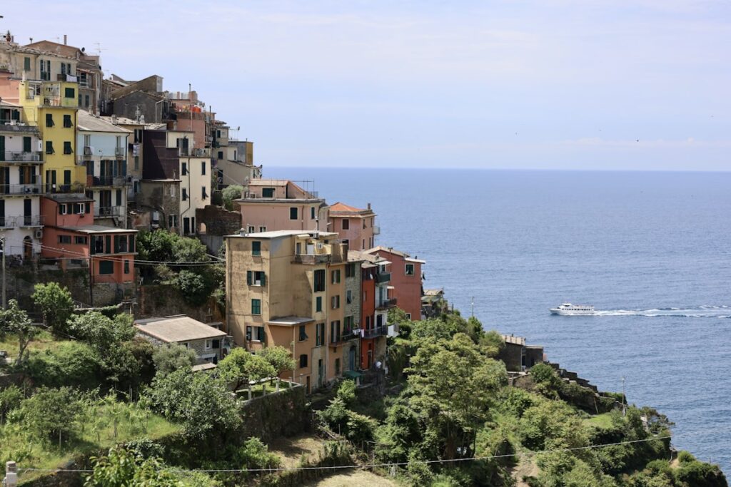 Casario colorido na encosta íngreme de Corniglia, com um barco a navegar no mar azul ao fundo