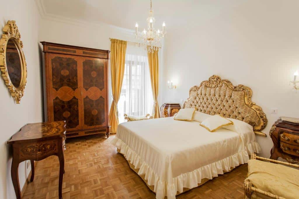 quarto da Suite Sarandrea, um alojamento local em Roma, com cama enorme e decoração clássica, mesa e candeeiros de ambos os lados, um lustre por cima, roupeiro e móveis de madeira e uma janela grande com cortinas