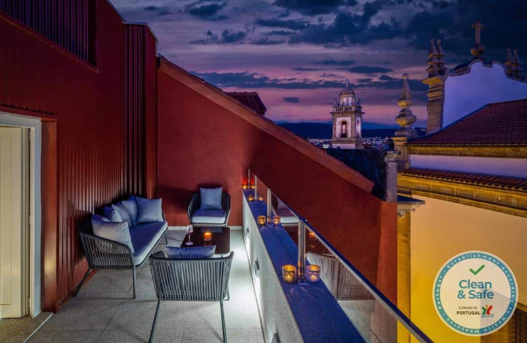 Varanda do Hotel Moon & Sun Braga com assentos e velas, e vista para a cidade ao anoitecer, com uma torre de igreja ao fundo.