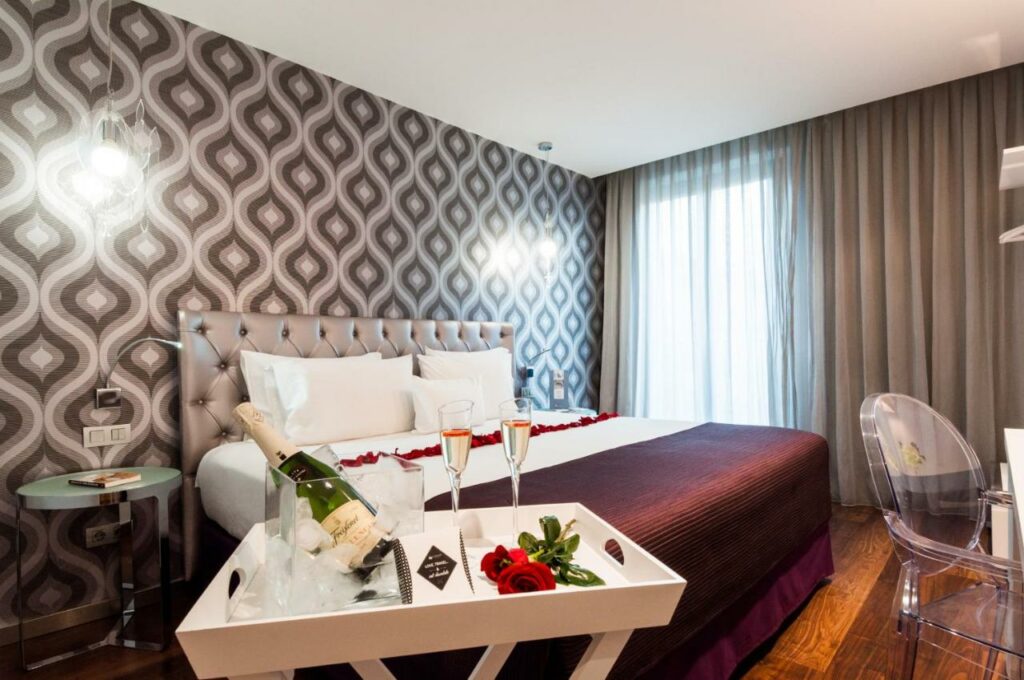 Quarto do Ikonik Ramblas, com decoração romântica, cama de casal com rosas, uma bandeja com champanhe num balde e duas taças, mesas de cabeceira e secretária.