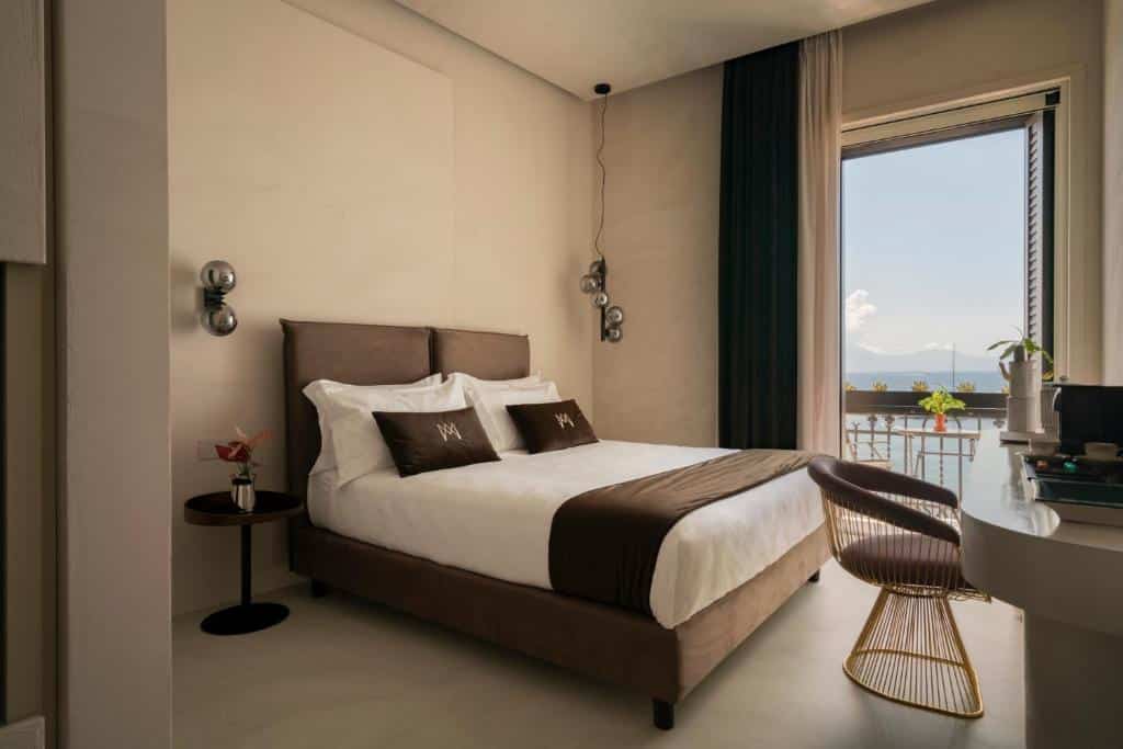 Quarto do Demetra Luxury Suites com cama de casal, cortinas escuras, cadeira de design moderno e bela vista panorâmica através da janela.