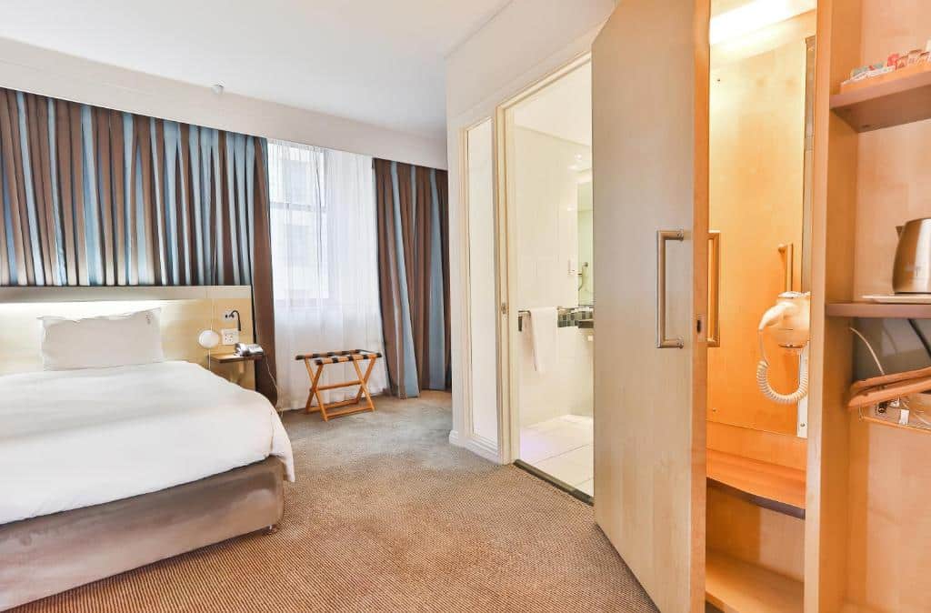 Quarto do Holiday Inn Express com cama, janela, armário aberto e entrada da casa de banho com azulejos brancos.
