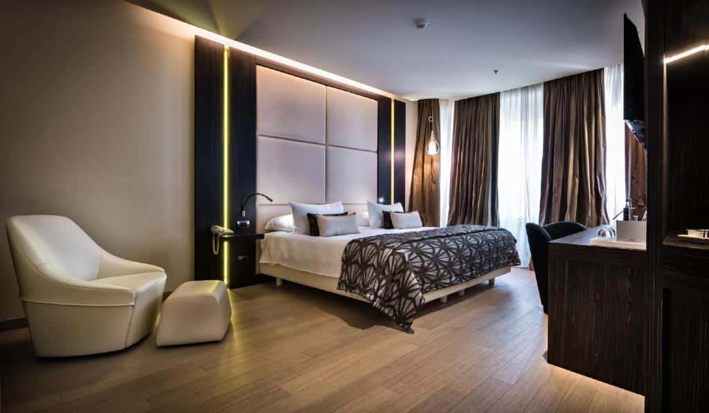 Quarto amplo com cama de casal, poltrona branca com apoio de pés e janela grande no The Square Milano Duomo