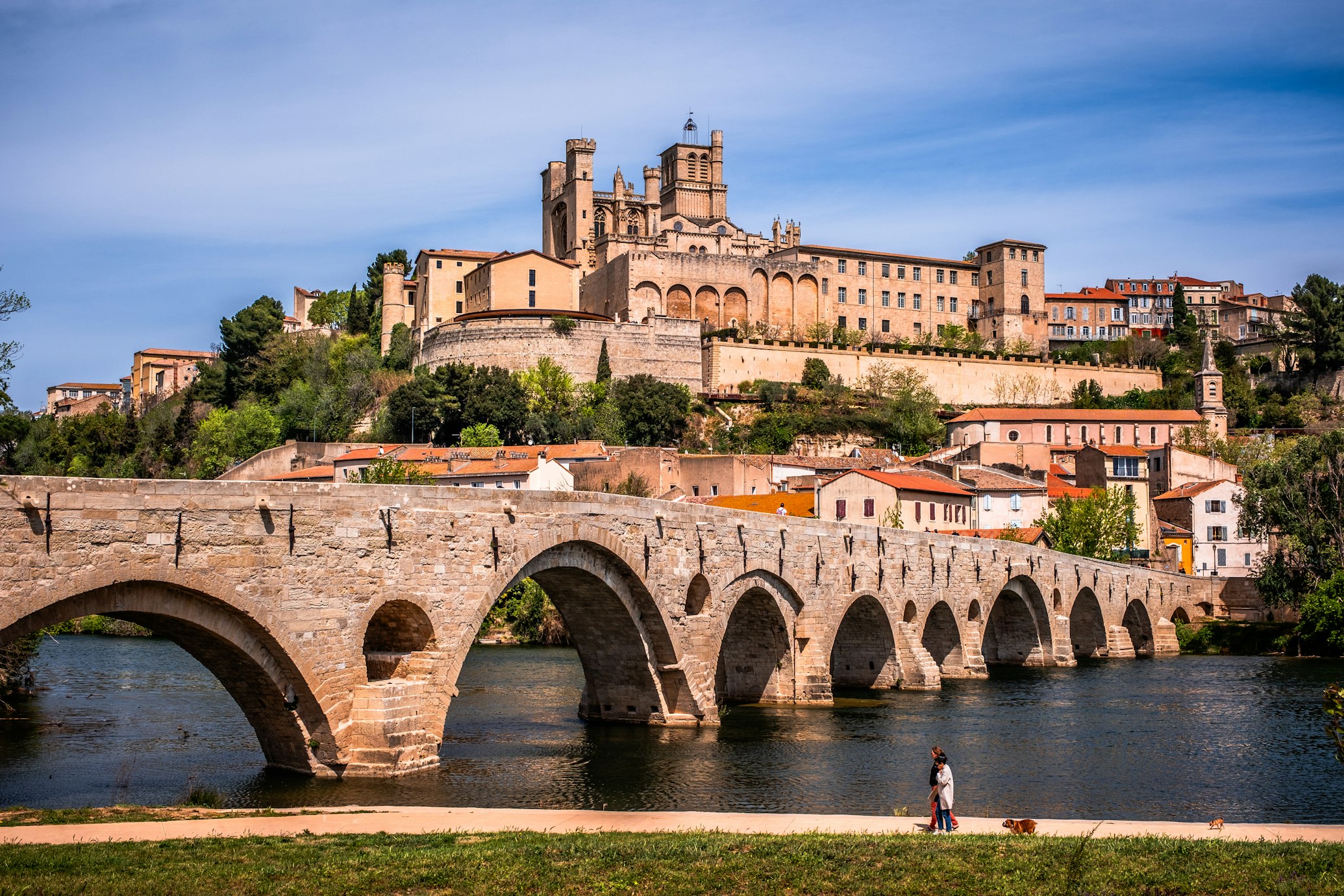 Ponte em arco de pedra sobre um rio, com uma catedral histórica e edifícios numa colina ao fundo, em Béziers.