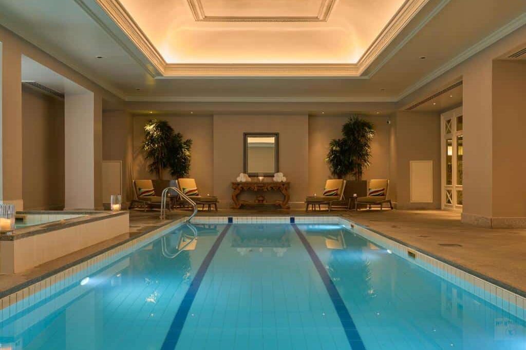 No InterContinental Dublin by IHG, uma piscina interior de luxo com espreguiçadeiras e plantas ornamentais num ambiente sofisticado de teto alto.